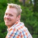 Man in plaid shirt pictured with book cover of "Mysteries of the National Parks"
