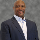 Smiling man in a suit with a gray background.