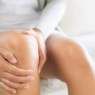 woman sitting on sofa and feeling knee pain