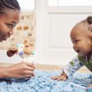 mother holds stuffed animal for baby on blue blanket