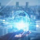 Abstract image of a transparent globe hovering over an open hand against a blue background. 