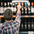 Man in a plaid shirt with his back facing the camera is reaching for a bottle of wine on a store shelf. UC Davis researchers say a variety of factors are causing the recent dip in wine consumption.  (Getty)