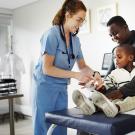 Doctor wrapping gauze on injured boy's hand with father comforting in clinic