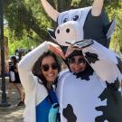 Two people make a heart shape with their arms. One is dressed in an inflatable cow costume.