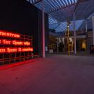Neon sign, in orange, photographed at dusk in front of museum