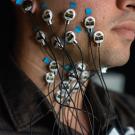 Side view of a young man's face from upper chest to chin. Attached to the skin are several small round disks with wires attached. 