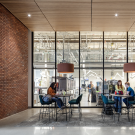 A cozy indoor workspace with dark wood accents and seating, featuring students engaged in conversation against a laboratory backdrop. 
