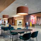 Modern lobby with light fixtures, tables and seating areas, and people interacting. A reception desk has a "300 Aggie Square" banner on it.