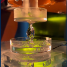 A translucent curved shape above a dish of liquid with some green color below. The image is framed by blue bars. 