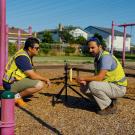 Two men in yellow construction vests squat on a schoolyard playground