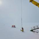 three researchers in coats and a yellow robotic glider are on the ice and snow in Antarctica next to a yellow crane