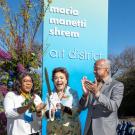 Three people having cut a ribbon with a large scissors in front of Manetti Shrem sign
