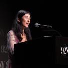 A young woman stands at a podium in a dark room