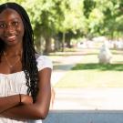 Student stands with her arms crossed with campus in the background