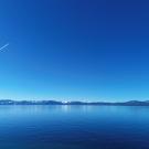 A plane's contrails streaks through a blue sky over deep blue Lake Tahoe