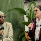 Fatima Denton,left, hold microphone and turns head to Tessa Hill, who is speaking into microphone. A green background and plant are behind them with the words We Don't Have Time printed on backdrop.