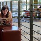 : A student lies on a padded bench inside the UC Davis Student Community Center and works on their laptop.