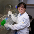 A woman wearing a University of California lab coat works with samples in a laboratory environment