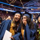 Students in graduation caps and gowns react in surprise and joy and streamers fall from above at an undergraduate commencement at the Golden 1 Center in June 2025. 