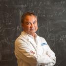 Photo of person in lab coat standing in front of chalkboard