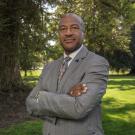 Chancellor Gary S. May stands in front of a tree on the Quad, with his arms crossed.