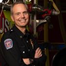 Fire chief stands in front of a fire truck with arms crossed.