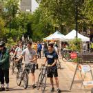 People walk their bicycles down Third Street, with views of UC Davis in the background.