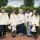 Five individuals in matching outfits stand in a garden filled with colorful flowers.