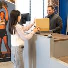 A woman hands a package to a smiling man at a service counter in a modern office setting.