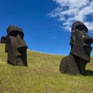 Two massive stone carvings of heads stand on a grassy field under bright blue skies.