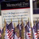 American flags displayed next to a sign that reads UC Davis Memorial Day Ceremony: These 136 flags serve as a tribute to the fallen Aggies who gave their lives in service to their country. Each flag represents a fallen Aggie.