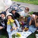 A diverse group of five Aggies enjoying a picnic on an Egghead blanked with Egghead merchandise in front of the Eye on Mrak Fatal Laff Egghead sculpture