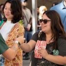 Smiling woman in sunglasses holding popcorn at a crowded outdoor gathering