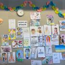 A wall in the ArtSpark studio filled with drawings left by other visitors. The drawings include self-portraits, landscapes, and other abstract shapes.