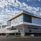 Photo shows exterior of 48X building, with UC Davis Health logo prominently visible, under bright blue sky filled with clouds.
