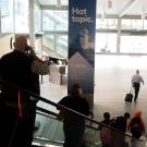 People descend an escalator at the Sacramento International Airport next to an ad for UC Davis’ Unfold podcast.