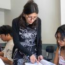 Student helps high schoolers with work in a classroom