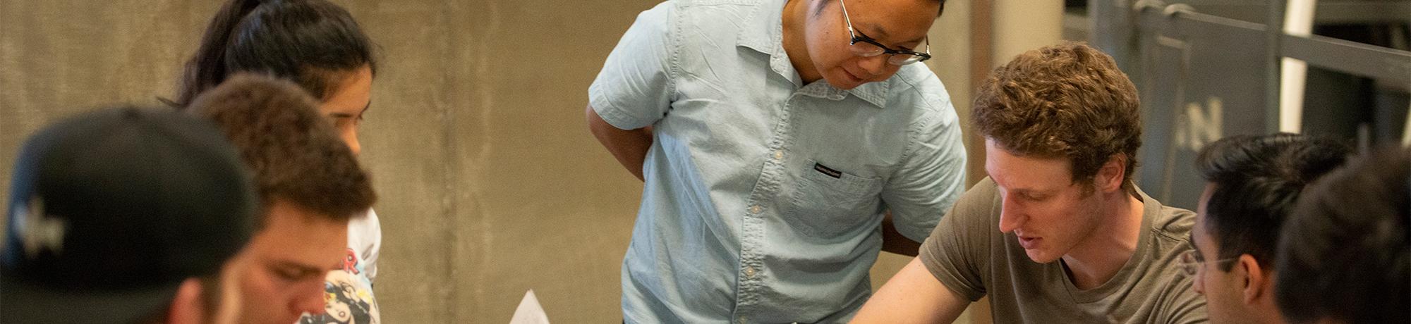 A teaching assistant leans over to assist a student during an engineering class.