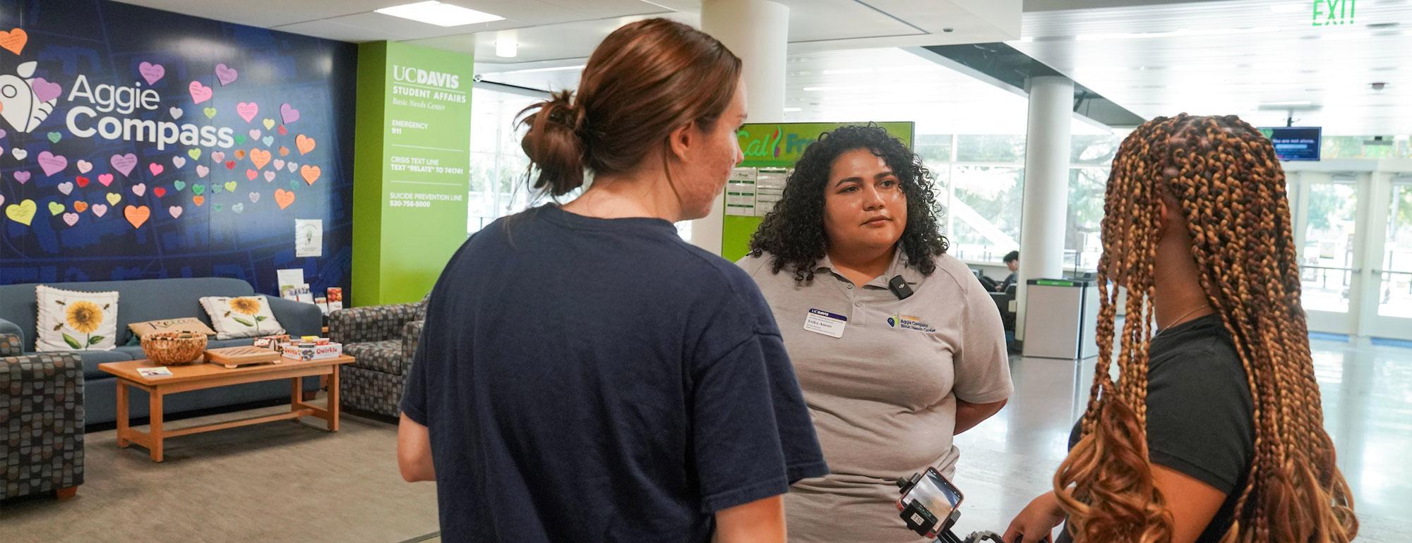 The interior of the Aggie Compass Basic Needs center featuring three people discussing the center's services