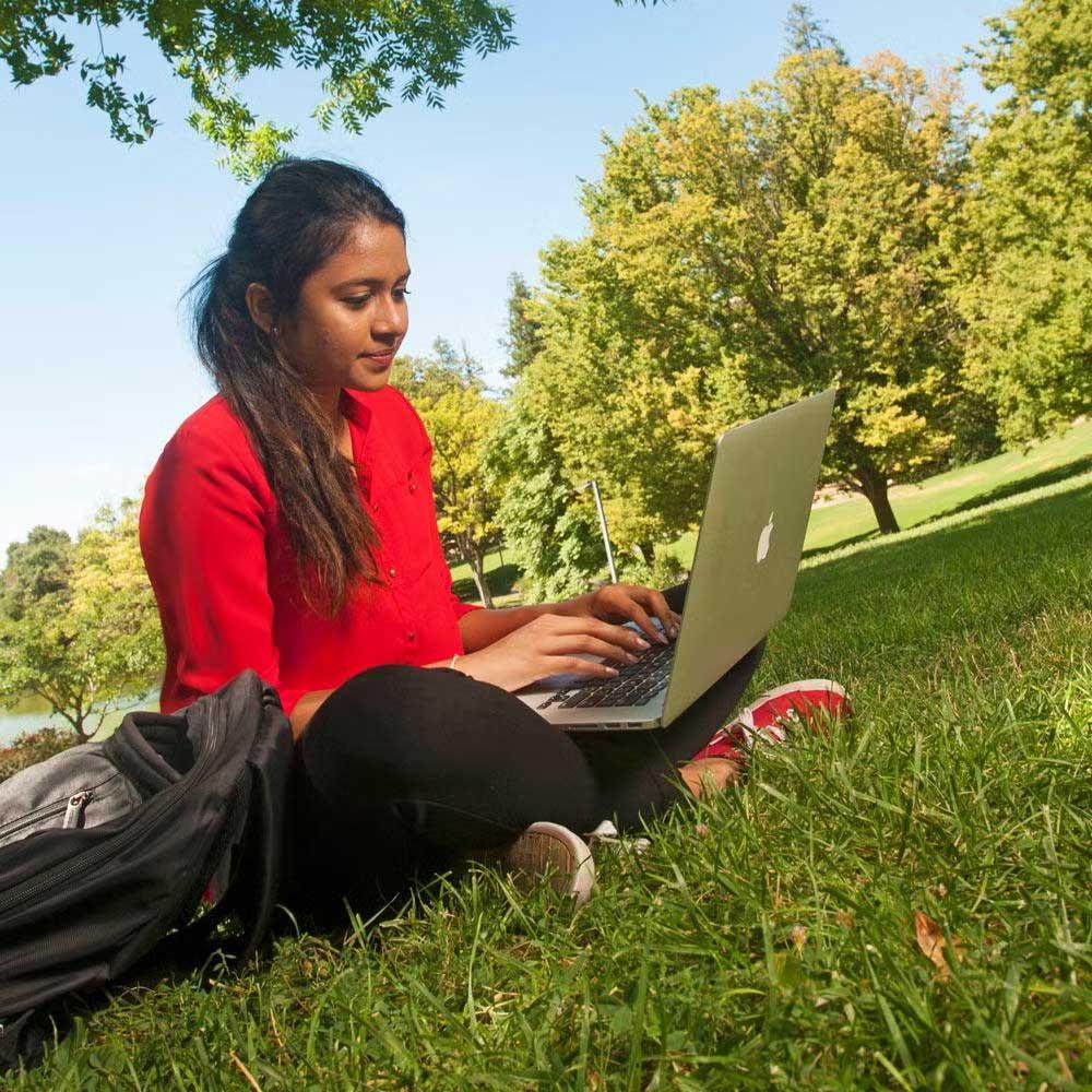 Girl studying on grass with laptop
