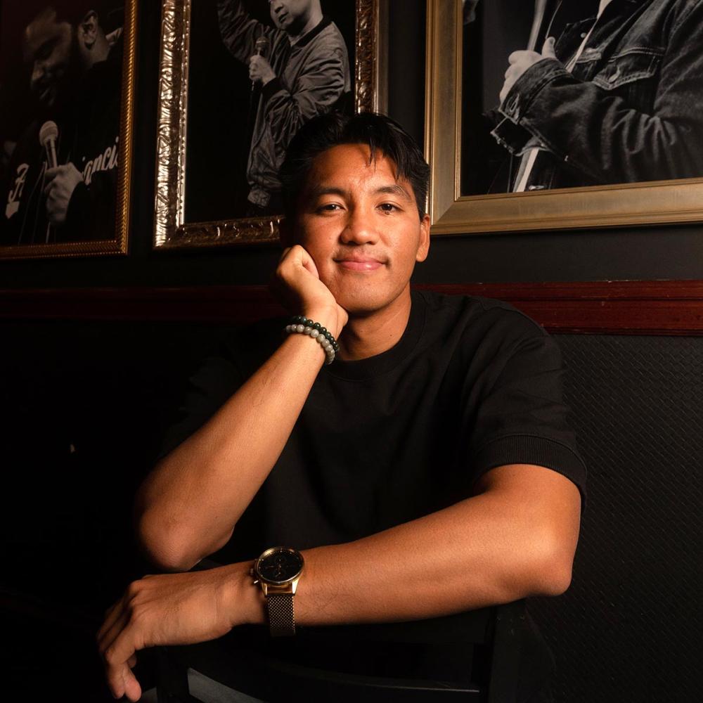 Photo of a man sitting and looking at the camera, smiling, with arms folded.