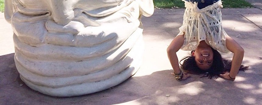 Woman performing handstand next to an upside down egghead statue