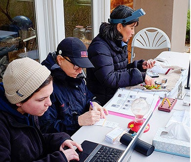Three women sit at a table with books and other paraphernalia
