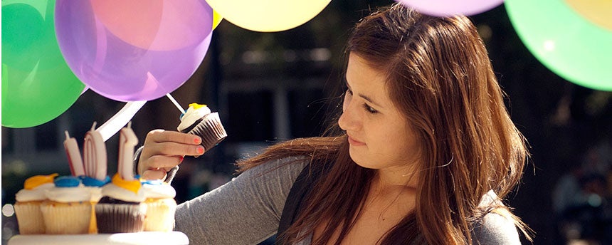 Young woman picks up frosting-covered cupcake.