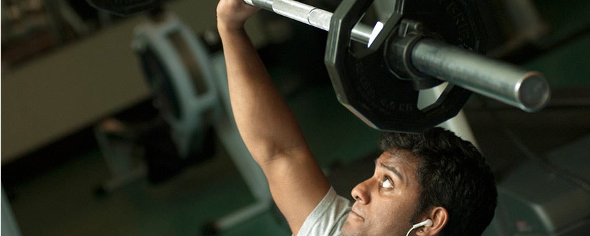 Male college student looks up at weight he is lifting.