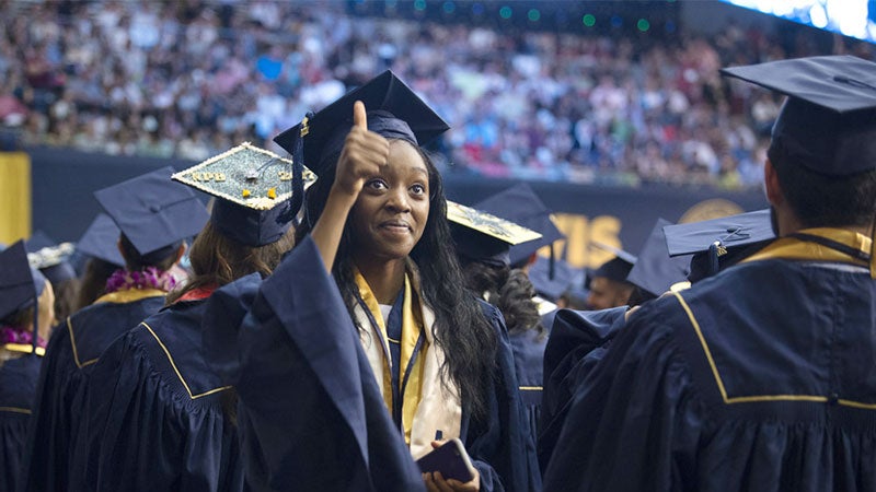 A female graduate gives a thumbs up at commencement